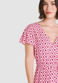 Vestido rosa con estampado de diamantes blancos; presenta mangas cortas y ligeras y un escote en V profundo; la tela parece ligera y suave.