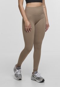 Leggings beige de talle alto hechos de una tela elástica, con una textura suave y un diseño sin costuras. Llevados con zapatillas deportivas grises.