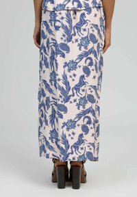 Jupe maxi en tissu rose clair avec un motif floral et animal bleu, dotée d'une silhouette droite et d'un ourlet évasé. Chaussures à talons hauts marron.