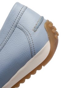 Talons de baskets en cuir bleu clair avec surpiqûres visibles et semelle en caoutchouc marron avec grip texturé sur fond blanc.