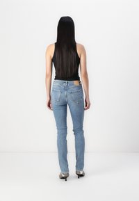Jean en denim bleu avec une coupe ajustée, présentant une taille mi-haute, des jambes fuselées et deux poches arrière. Associés à des chaussures à talons.