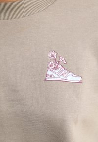 Sweatshirt bej cu guler ribbat, având o ilustrație imprimată a unei teniși cu accente de flori roz și un design detaliat al pantofului.