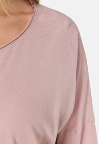 Hellrosa, übergroßes T-Shirt mit weitem Halsausschnitt, aus weichem Baumwollstoff und tiefen Schulternähten, mit einer glatten, unifarbenen Textur.