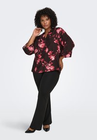 Black floral long-sleeve blouse with pink flower patterns, v-neckline, and relaxed fit. Paired with black slim-fit pants and pointed-toe heels.