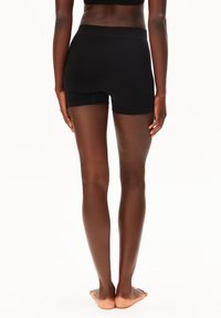 Shorts noirs ajustés avec une large ceinture élastique, texture lisse, sans coutures visibles, arrivant à mi-cuisse sur des jambes nues.