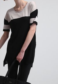 Haut noir et argent métallique à manches courtes, avec un design color block et une coupe décontractée. Le tissu a une texture lisse.