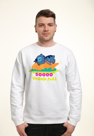 Mann trägt weißen Pullover mit einer Zeichentrickfigur eines blauen Wesens, das auf einem gebratenen Truthahn schläft, und dem Text „soooo dank-bar.“