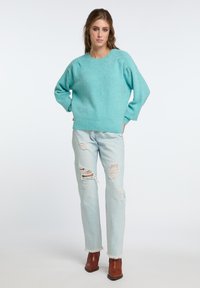 Maglione turchese a maglia con scollo rotondo e vestibilità morbida; abbinato a jeans chiari strappati e stivaletti marroni.