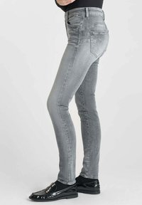 Jean skinny gris avec une texture lisse, doté de cinq poches et d'une taille classique. Associé à des mocassins noirs brillants.