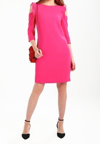 Robe fuchsia à épaules découvertes avec manches à volants, longueur genou, texture lisse. Associée à un sac rouge et des chaussures à talons noirs.