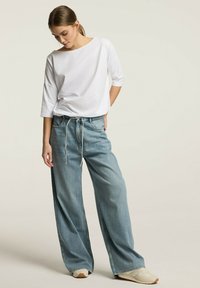 Biała bluzka z szerokim dekoltem i rękawami 3/4, zestawiona z luźnymi, jasnoniebieskimi spodniami dżinsowymi o wysokim stanie, z elastycznym pasem ze sznurkiem.