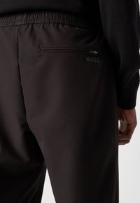 Colanți negri cu talie elastică și un buzunar cu fermoar. Prezintă un logo discret "BOSS" într-o culoare contrastantă. Textură netedă.
