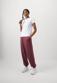 T-shirt bianco di cotone con maniche corte e logo piccolo, abbinata a pantaloni morbidi bordeaux con tasche laterali e un emblema ricamato.