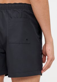 Shorts de bain noirs en tissu léger, dotés d'une taille élastique, d'une poche arrière avec un bouton et d'une texture lisse.