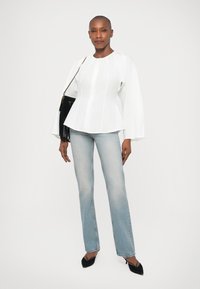 Top peplum branco de manga longa com detalhes franzidos, combinado com jeans claros de corte flare e sapatos de salto agudo pretos. Bolsa preta com franjas.