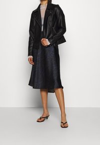 Giacca da motociclista in pelle nera, top grigio trasparente, gonna a linea A con motivo blu e tacchi neri con cinturini. Texture lisce e design a strati.