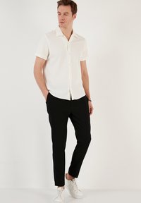 Hvid kortærmet skjorte med ribbet tekstur, sort slim-fit bukser og hvide sneakers. Enkel krave og knaplukning foran.