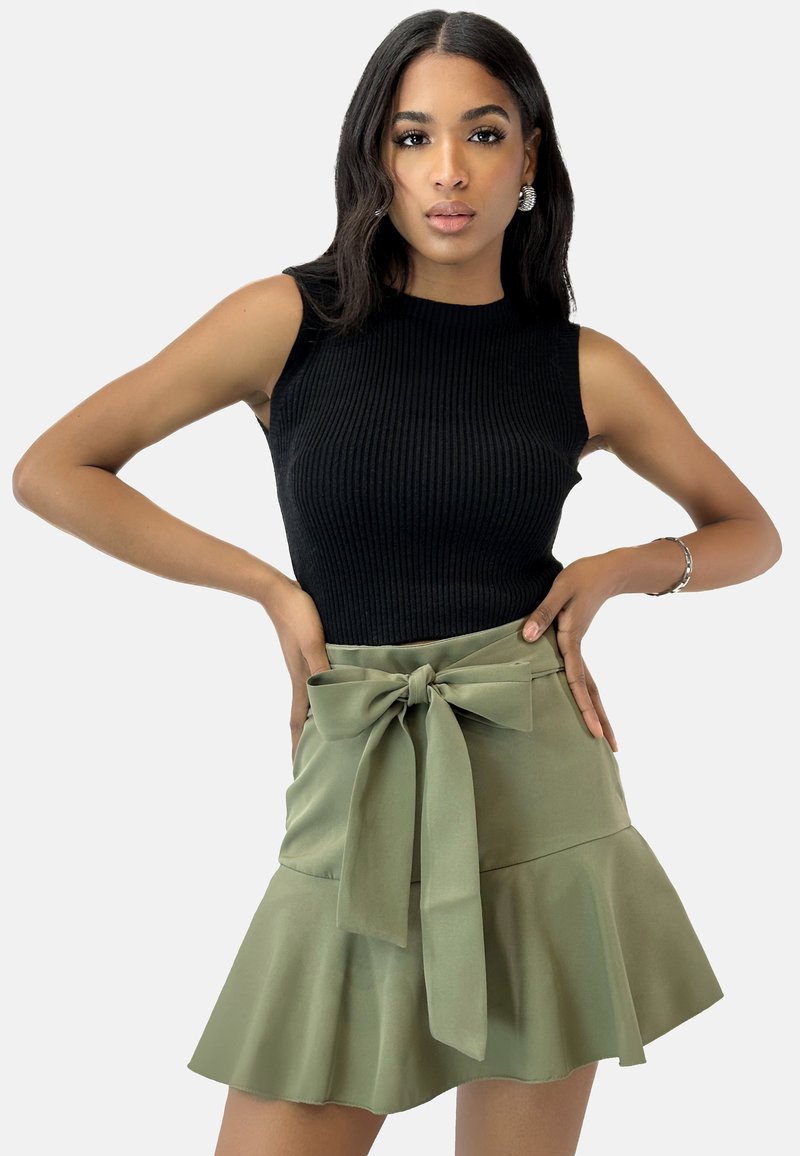 Top sin mangas negro con canalé, combinado con una falda verde acampanada que presenta un cinturón anudado en la cintura. Tejido suave, forma estructurada.