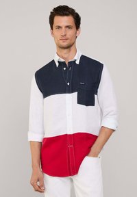 Camisa de botones de manga larga con bloques de color en azul marino, blanco y rojo. Fabricada en lino, con un bolsillo en el pecho, puños enrollados y dobladillo curvado.