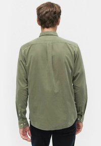 Oliivinvihreä, pitkähihaista paitaa pehmeästä kankaasta, jossa on rento leikkaus, kärkipaitakaulus ja napitettavat hihansuut. Yksityiskohtiin kuuluu keski-hihansuu.