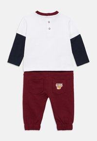 Σετ ρούχων για νήπια από βαμβάκι, που περιλαμβάνει λευκή μπλούζα με μπλε μανίκια και μπορντό γιακά, σε συνδυασμό με μπορντό παντελόνι με λογότυπο αρκούδας στην τσέπη.