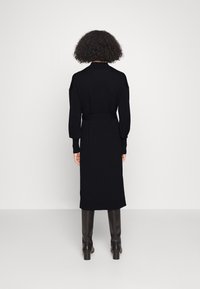 Robe tricotée noire avec des manches longues, une taille ceinturée et une longueur midi. Texture lisse et design simple et épuré.