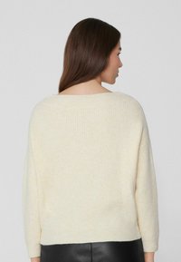 Cremfarbener, gerippter Strickpullover mit lockerer Passform, Bootsausschnitt und Dreiviertelärmeln, kombiniert mit einem dunkel, eleganten Lederunterteil.