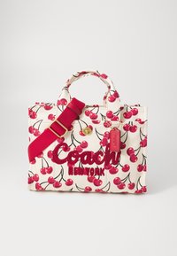 Plátená taška s krémovým pozadím, potlačou červených čerešní a vyšívaným nápisom "Coach NEW YORK." Má červené uši a nastaviteľný popruh.
