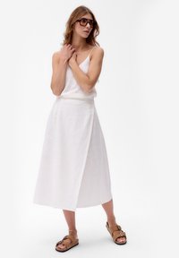 Witte linnen wraprok met een A-lijn silhouet. Gecombineerd met een mouwloos wit topje met een subtiele meshpatroon en bruine sandalen.