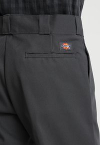 Närbild av svarta Dickies-byxor med bakfickan och logotypen ovanför ficköppningen samt breda bältesöglor på midjan.