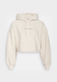 Felpa con cappuccio corta color crema in tessuto morbido e testurizzato. Presenta un cappuccio con coulisse e polsini a costine, con un logo stampato sul davanti.