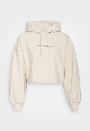 Cropped hoodie in crèmekleur met een zachte, gestructureerde stof. Voorzien van een capuchon met trekkoord en geribbelde manchetten, met een logo op de voorkant gedrukt.