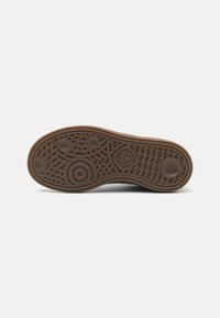 Brown rubber shoe sole with textured patterns, featuring circular and wavy designs, and a small logo at the heel.