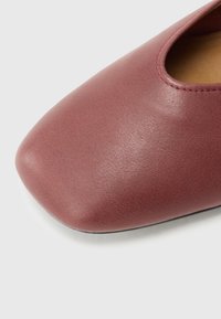 Pantof slip-on din piele maro roșcată, cu vârf rotunjit, pătrat și detalii minime de cusătură, evidențiind o textură netedă și un luciu subtil.