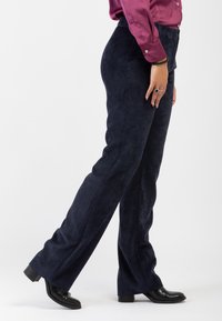 Pantaloni in corduroy blu navy con design a gamba dritta, caratterizzati da una fine texture a righe e una vita piatta, abbinati a stivali neri alla caviglia.