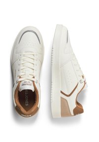 Weiße Ledersneaker mit beigen Akzenten, strukturierten Seiten, flachen Schnürsenkeln und einer abgerundeten Zehenpartie. Perforationen und das Markenlogo sind auf der Zunge sichtbar.