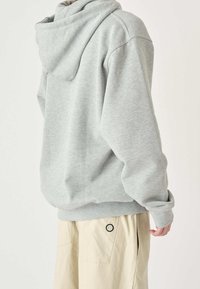 Grå hoodie i mjukt, texturerat tyg med dragsko på huvan. Har en avslappnad passform och ribbade muddar, ihop med beige byxor.