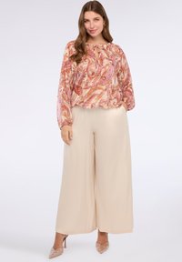 Hladká blůza v růžovém a béžovém paisley vzoru s klíčovou dírkou na výstřihu, spárovaná s béžovými kalhotami s širokými nohavicemi a béžovými podpatky.