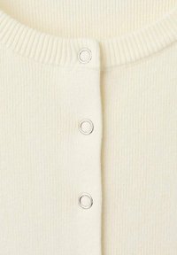 Suéter de punto en crema con cuello redondo y tres botones de presión plateados en el frente. Textura suave con detalles finos.