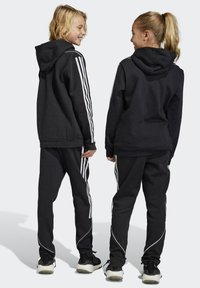 Haut à capuche noir et pantalon assorti avec des rayures blanches sur les côtés. Le tissu semble doux et durable, avec une capuche à cordon de serrage et une coupe décontractée.