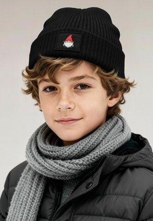 Black knitted beanie featuring a gnome design on a patch; paired with a thick gray knit scarf. The jacket is black and padded.