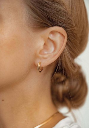 Gold hoop earring with a textured surface and a small studded accent. The earring is worn on a model's ear with light brown hair.