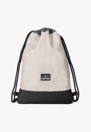 Repunapitasku dalam warna krim dan hitam, terbuat dari kain yang tahan lama. Memiliki tekstur halus, penutupan serut, dan label logo hitam di bagian bawah.