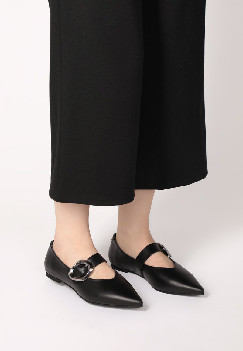 Černé kožené baleríny s špičatou špičkou, páskem přes nárt a dekorativní metalickou přezkou. Matný povrch a nízký podpatek.
