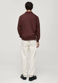 Sweat-shirt marron avec poignets et ourlet côtelés, associé à un pantalon blanc et des chaussures noires. La vue montre le dos de la tenue.