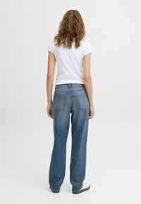 Jeans de mezclilla azul claro con un corte relajado, cinco bolsillos y una etiqueta de cuero en la cintura, combinados con una camiseta blanca.