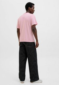 Lyserød bomulds T-shirt med korte ærmer, afslappet pasform og rund halsudskæring, parret med sorte denim bukser med vidde og kontraststikninger.