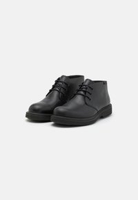 Botas de tobillo de cuero negro con una textura suave, puntera redonda y diseño de cordones. Suelas de goma y forma minimalista. Sin patrones visibles.