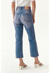 Džínsy z denimu v svetlom modrom prevedení, s rovnými nohavicami a vysokým pásom, s hnedou koženou nášivkou. Obsahujú dva zadné vrecká a viditeľné švy.