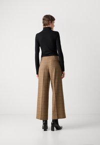 Bruna rutig högmidjad byxor med vida ben, texturerat tyg, bakfickdetalj, tillsammans med en figurnära svart polotröja och svarta klackboots.
